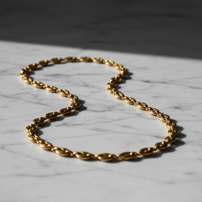 Aramat Jewels goudkleurige stalen koffieboon ketting van 4,5mm breed, een robuuste unisex schakelketting op marmer.