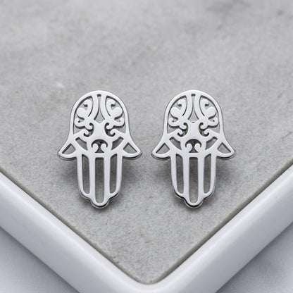 Aramat Jewels zilverkleurige Hamsa hand oorknopjes van RVS met een glanzende afwerking op een grijze ondergrond.