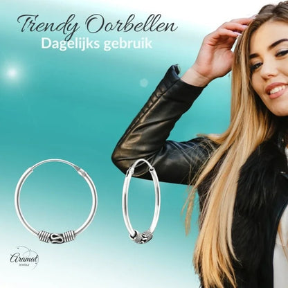 Aramat Jewels oxidized silver Bali hoop earrings, 20mm diameter, with intricate tribal detailing. Model wearing a black leather jacket.